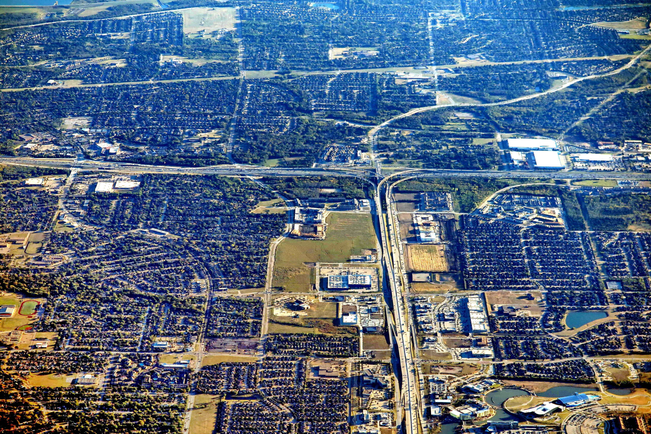 High-angle aerial view of a suburban commercial corridor with highways, retail centers, and residential neighborhoods.